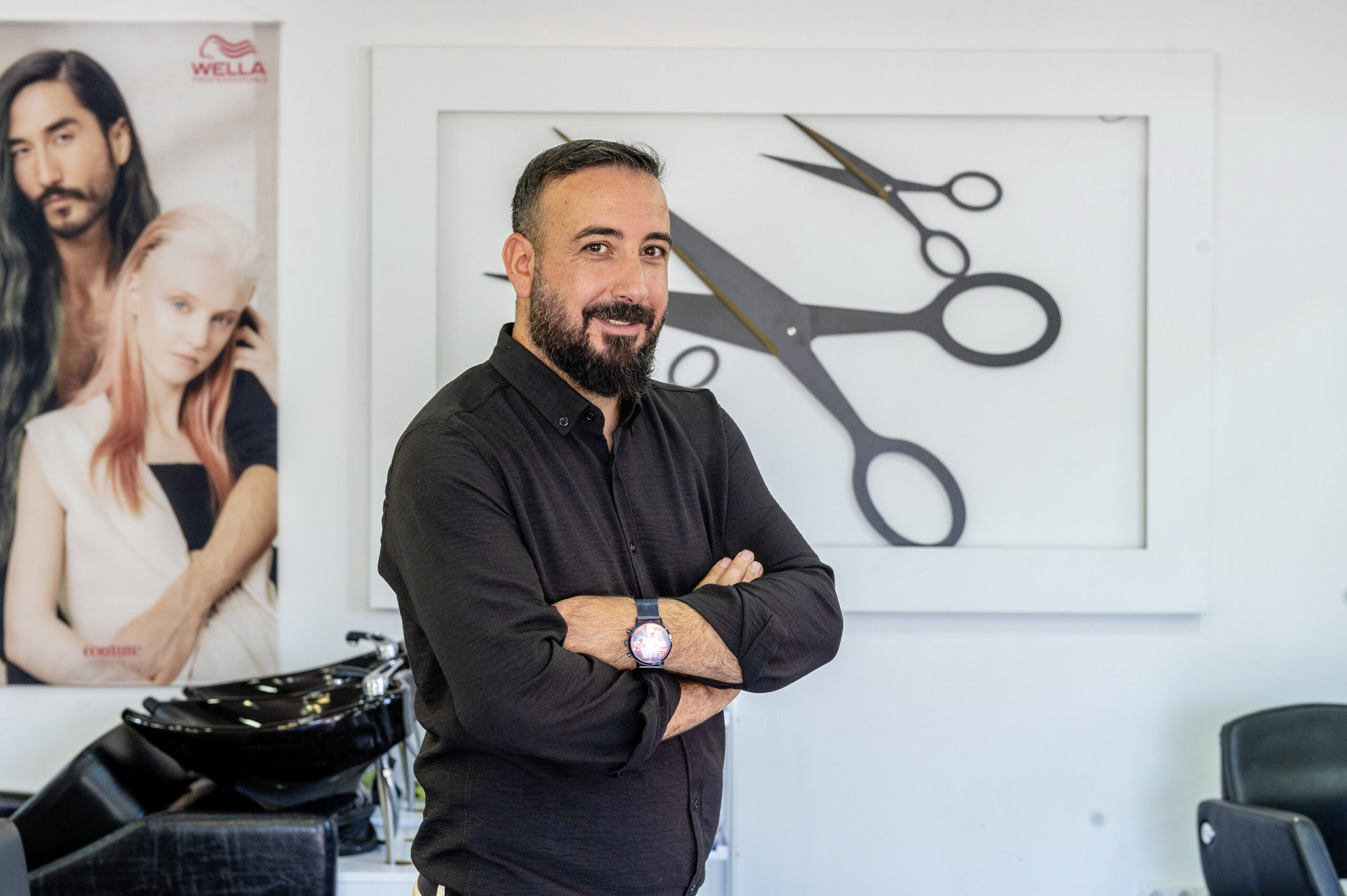 Porträt von Hasret und Abdullah Sari in ihrem Friseursalon vor einer Wand mit Scheren-Grafik.
