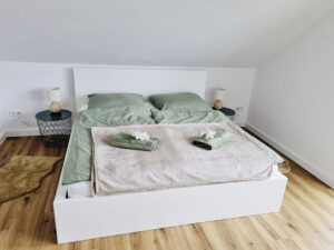 Ein helles, modern eingerichtetes Schlafzimmer im Dat Appelhus mit einem großen Doppelbett, hellgrauer Bettwäsche und Handtüchern sowie zwei Balkontüren im Hintergrund.