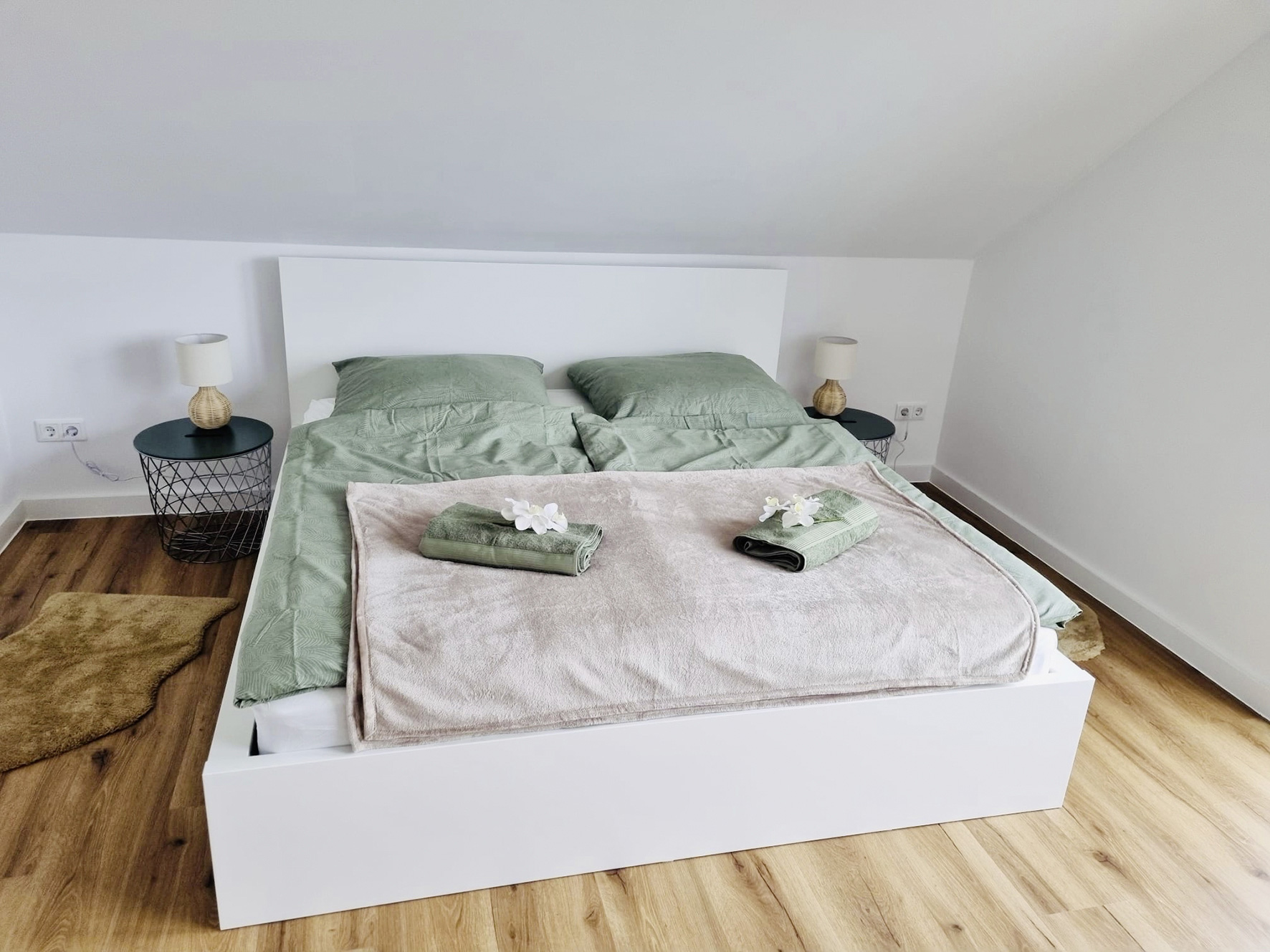 Ein helles, modern eingerichtetes Schlafzimmer im Dat Appelhus mit einem großen Doppelbett, hellgrauer Bettwäsche und Handtüchern sowie zwei Balkontüren im Hintergrund.