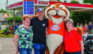 Drei Personen posieren mit einem Esso-Tiger-Maskottchen vor einer Esso-Tankstelle