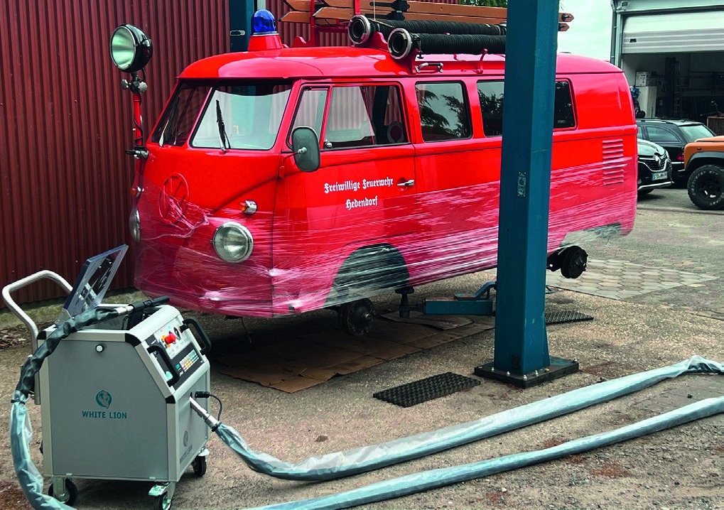 Roter VW T1 (Feuerwehr-Bulli) auf Hebebühne in einer Werkstatt, davor ein Trockeneisstrahlgerät mit Schläuchen
